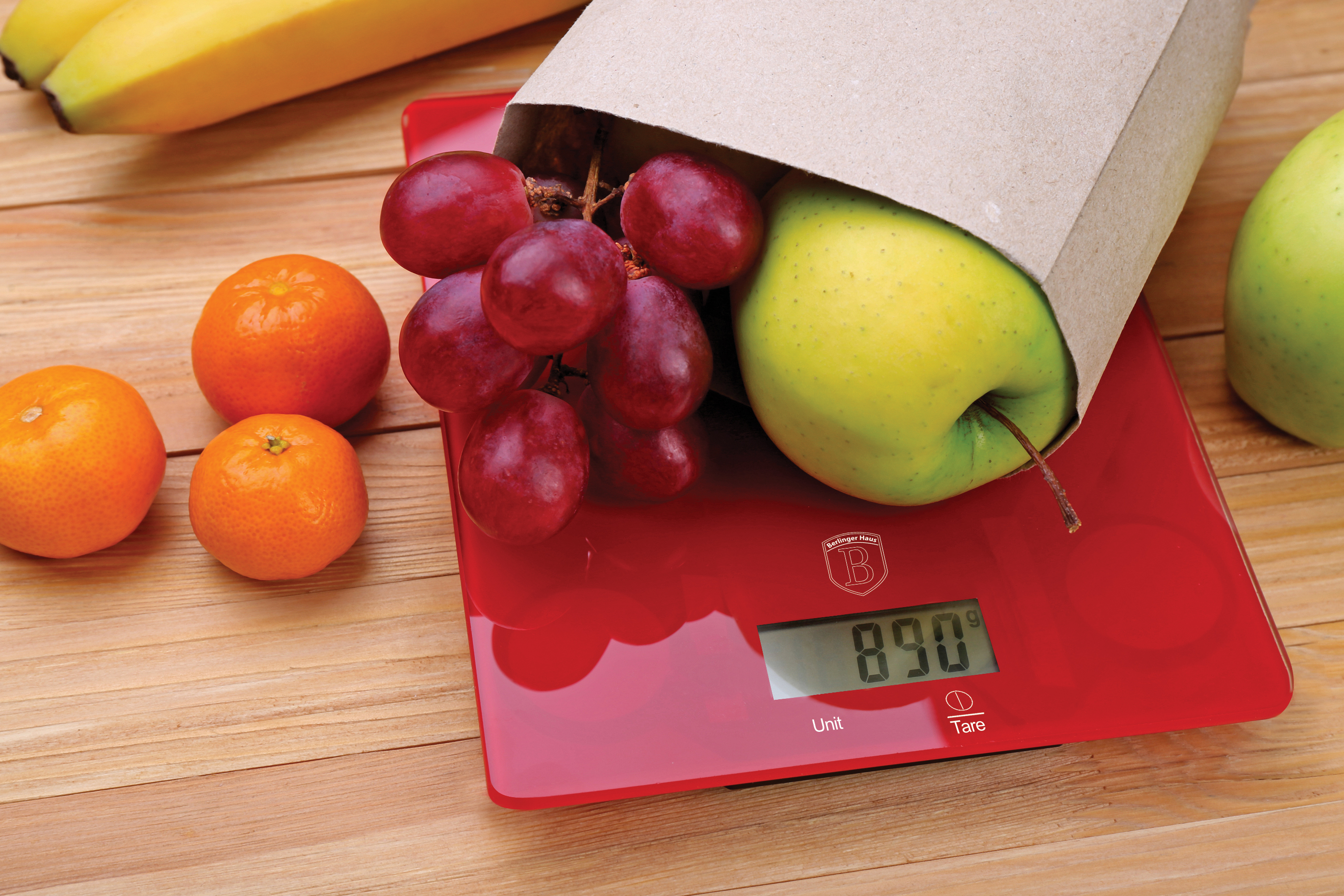 Fresh fruits on red digital kitchen scales over wooden backgroun